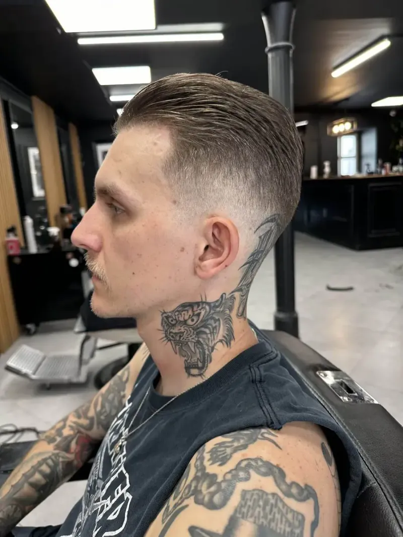 Krótkie męskie strzyżenie z wysoko poprowadzonym fade i gładko zaczesaną górą