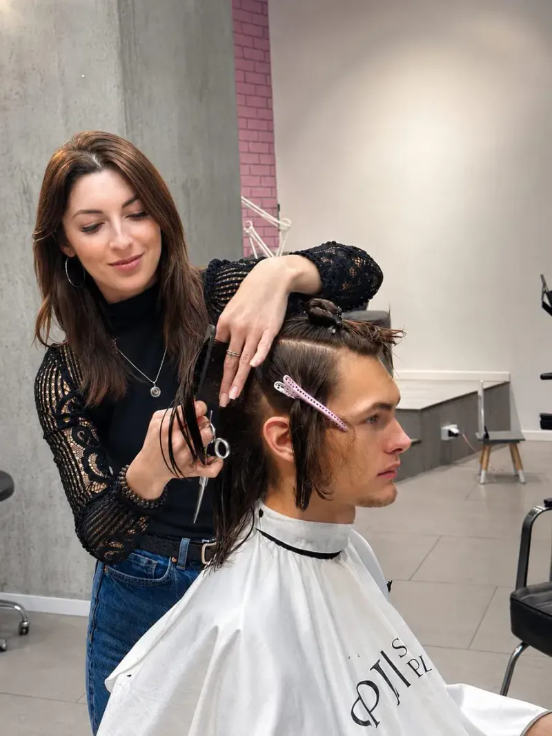 Barberka wykonuje precyzyjne strzyżenie dłuższych włosów klienta